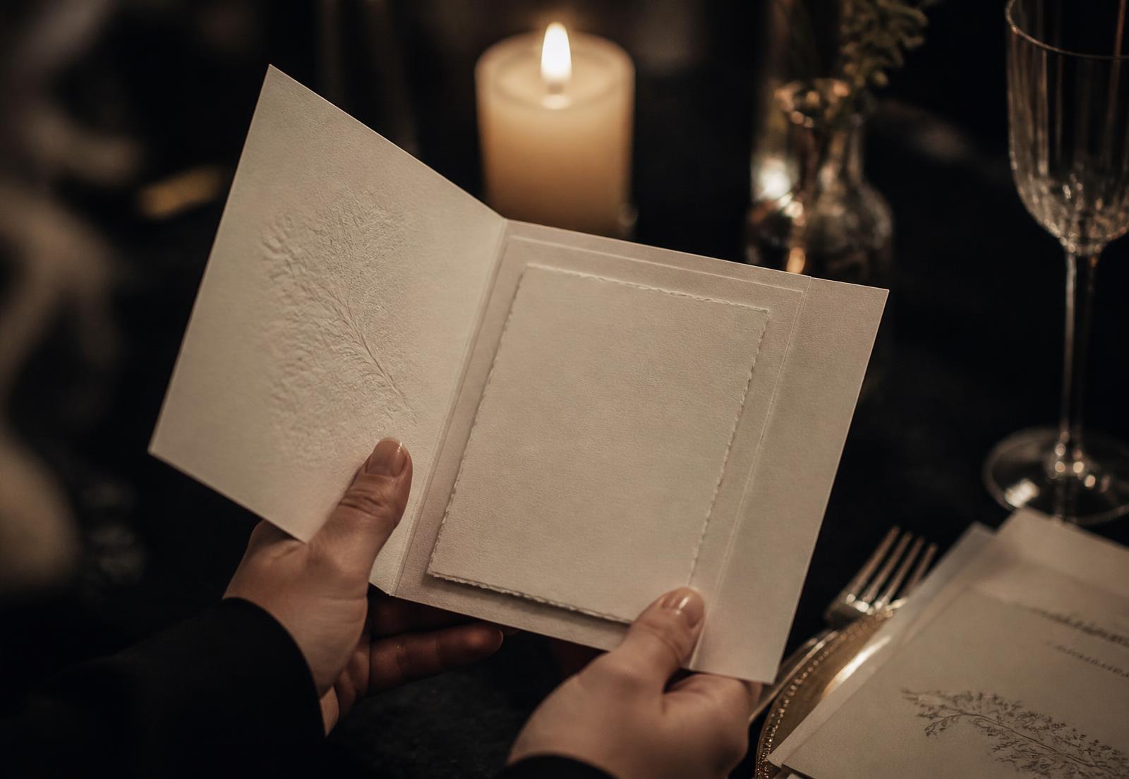 Hands holding an open letterpress invitation card by candlelight